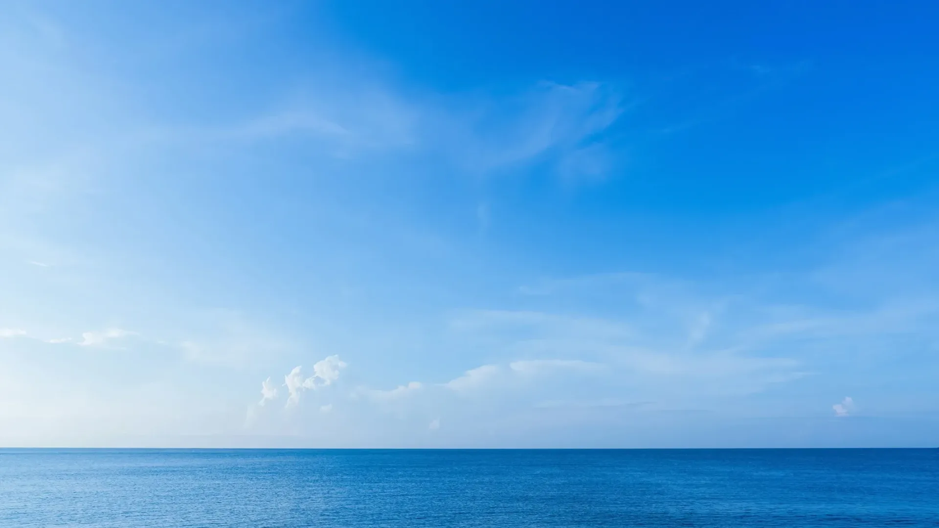 Radiant sun over a calm ocean with blue sky and white clouds